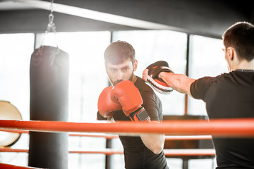 Athletic man fighting during the training with boxing trainer on the boxing ring at the gym