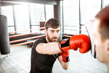 Athletic man fighting during the training with boxing trainer on the boxing ring at the gym