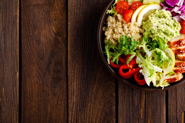 Buddha bowl dish. Healthy balanced lunch with quinoa, grilled chicken meat, lettuce salad, pepper, cucumber, tomato and avocado guacamole with lemon