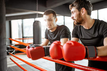 Two athletic men in black sportswear talking together, having fun during the break on the boxing ring at the gym