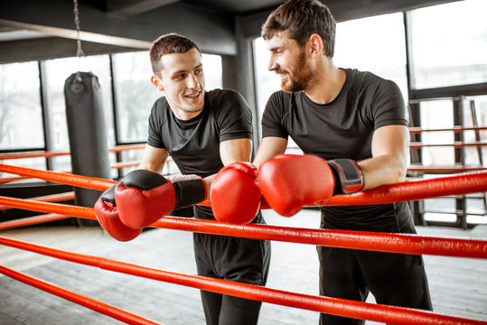 Two athletic men in black sportswear talking together, having fun during the break on the boxing ring at the gym