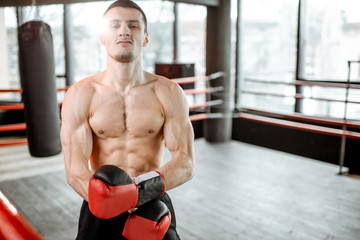 Portrait of a strong boxer showing muscles during the training on the boxing ring at the gym