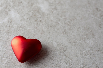 Fototapeta premium Close up of a single satin red heart with shadow on a tan background. Plenty of copy space. Background blurry.