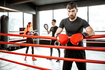 Man resting after the training on the boxing ring with people on the background at the gym