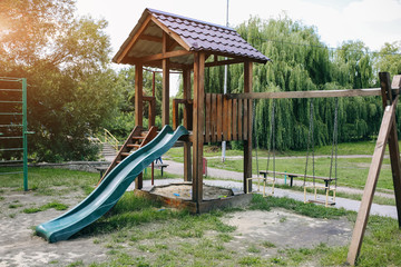 Slide and swings with a wooden house on children playground. Outdoors games for kids.
