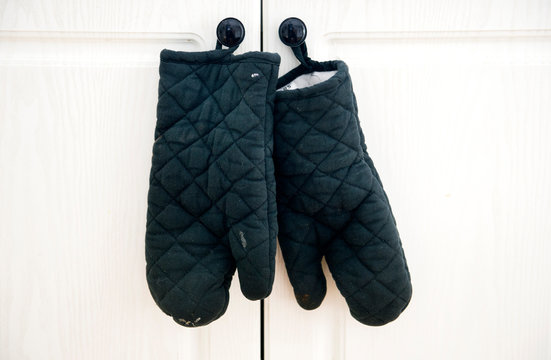 Worn Black Oven Gloves Are Shown Hanging From A Kitchen Cabinet