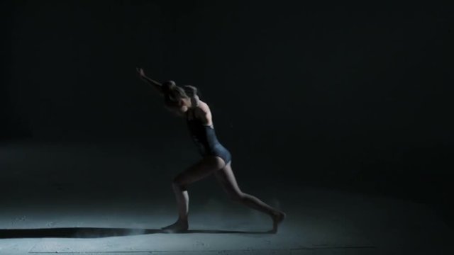 Barefoot Caucasian girl in black leotard performing modern dance 