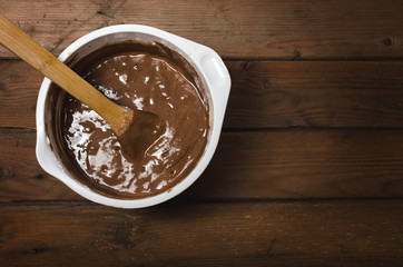 Cake pan with chocolate batter and wooden spoon close up on dark wooden background. Preparation of sponge cake.