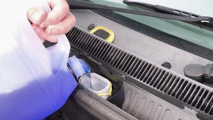 Caucasian, British male topping up the screenwash liquid in a small petrol car in England.