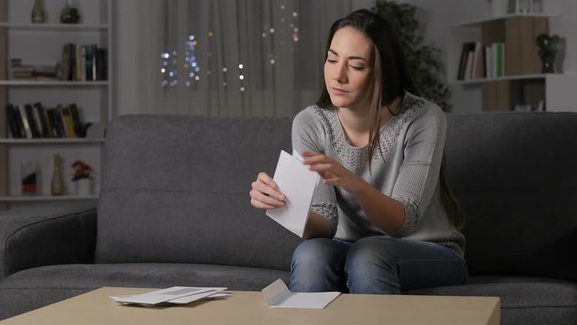 Excited woman reading good news on letter sitting on a couch in the living room at home