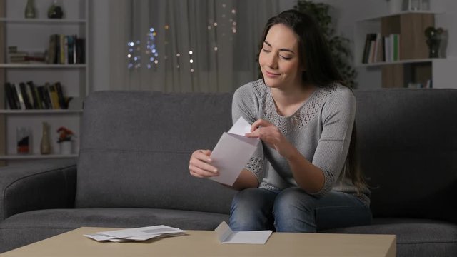Amazed woman reading good news on a letter sitting on a couch in the night at home