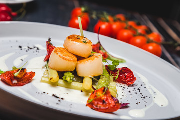 grilled scallop on a dark wooden background. The background is decorated with vegetables and spices.