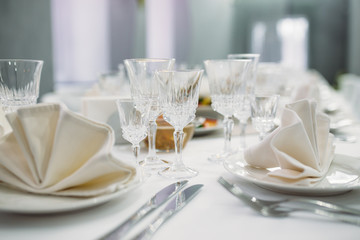 Luxury dinner set arranged on a table with vintage cream lace tablecloth and napkins, elegant porcelain dishes, silverware and crystal glassware