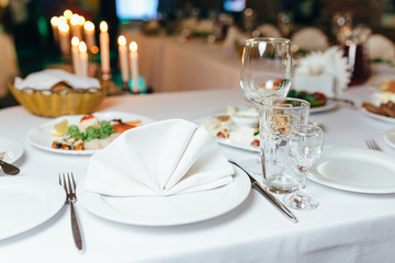 dinner set arranged on a table with vintage cream lace tablecloth and napkins, elegant porcelain dishes, silverware and crystal glassware