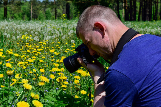 The young man takes photos of yellow flowers on the field.