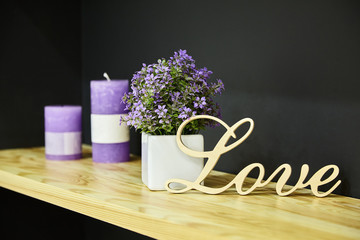 Home and restaurant decoration. Wooden word LOVE with candles and violet flowers on the dark background
