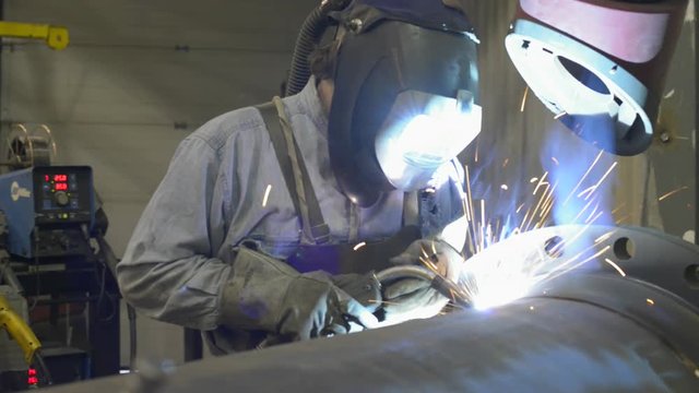 Sparks fly as a man welds a large pipe in an industrial machine shop