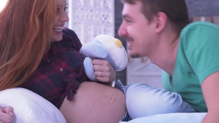 Beautiful pregnant woman and her husband lying on the bed and playing with soft toys. Dad kissing wife. Maternity concept. Pregnancy. Happy family. - Powered by Adobe
