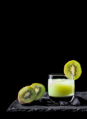 Kiwi juice with ice on black background and two pieces of kiwi