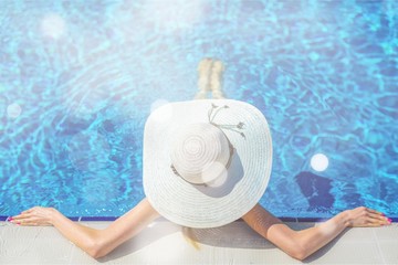 Beautiful woman in a hat sitting on the edge of the swimming