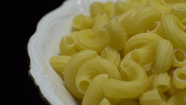 Raw macaroni in rotation. Elbow macaroni. Macaroni rigati close up.  Raw pasta  black background. Italian cuisine concept.