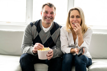 A Happy young couple lying on the sofa at home with popcorn watching TV