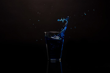 Glass blue drink splashing out. Shot against black reflective surface. Isolated beverage shot against black background. Copy space available