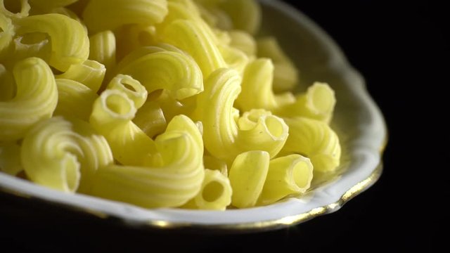 Raw macaroni in rotation. Elbow macaroni. Macaroni rigati close up.  Raw pasta  black background. Italian cuisine concept.