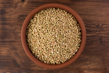 Natural fresh green buckwheat in clay bowl on wooden background. Top view