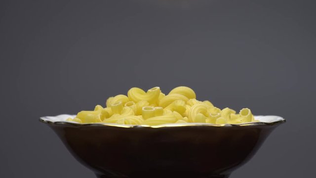 Raw macaroni in rotation. Elbow macaroni. Macaroni rigati close up.  Raw pasta  grey background. Italian cuisine concept.