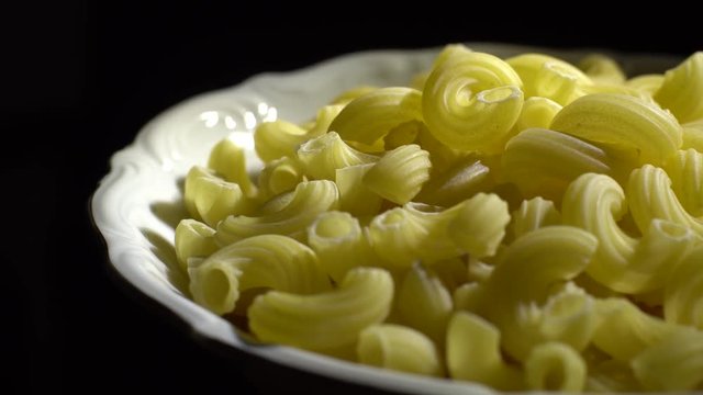 Raw macaroni in rotation. Elbow macaroni. Macaroni rigati close up.  Raw pasta  black background. Italian cuisine concept.