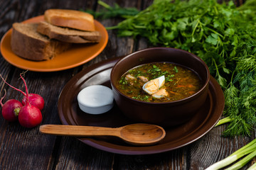 green borsch with egg and sour cream in a clay plate on a wooden table