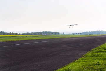 Unmanned aerial vehicle surveillance drone with light and camera landing on airport runway, ground, airfield, sunny summer morning, drone delivery concept, copy space on clear sky