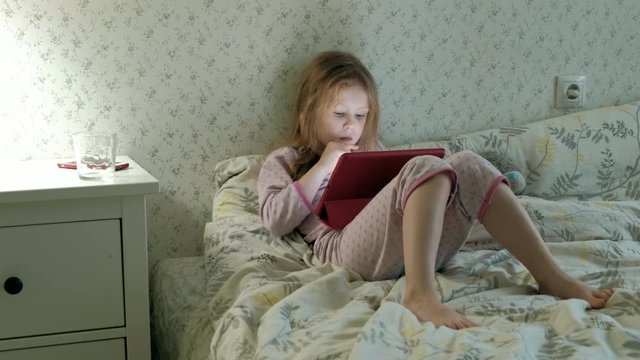 little girl in bed playing on tablet
