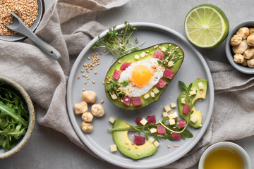 Keto diet dish: baked Avocado boat with ham cubes, quail egg and cheese served with green salad