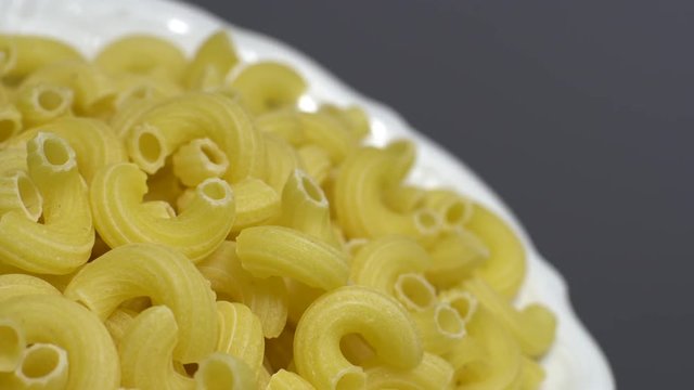 Raw macaroni in rotation. Elbow macaroni. Macaroni rigati close up.  Raw pasta  grey background. Italian cuisine concept.