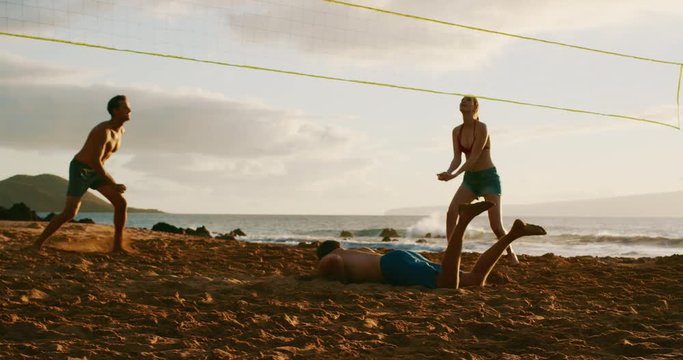 Group of friends playing beach volleyball at sunset, athletic man dives to save volleyball, slowmotion