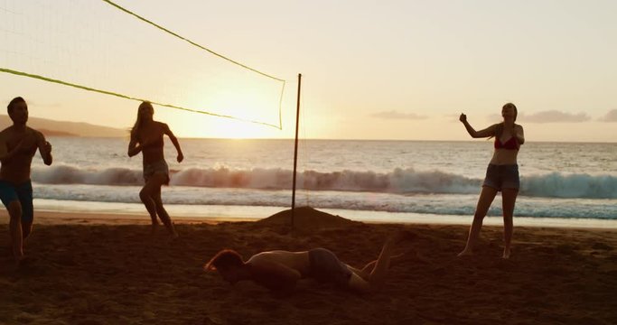 Group of friends playing beach volleyball at sunset, athletic man dives to save volleyball, slowmotion