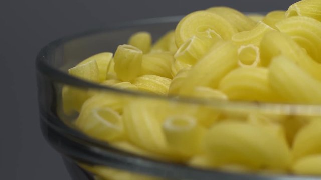 Raw macaroni in rotation. Elbow macaroni. Macaroni rigati close up.  Raw pasta  grey background. Italian cuisine concept.