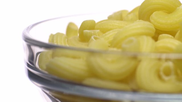 Raw macaroni in rotation. Elbow macaroni.  Macaroni rigati close up.  Raw pasta  isolated on white. Italian cuisine concept.