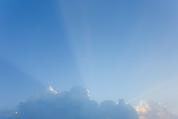 Beautiful morning blue sky background with soft long sunrays shining behind white fluffy cloud outside. Horizontal color photography.