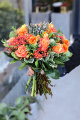 Beautiful bouquet in coral orange colors of roses, tulips, Jatropha multifida, Carthamus tinctorius and other plants in the male florist hand.