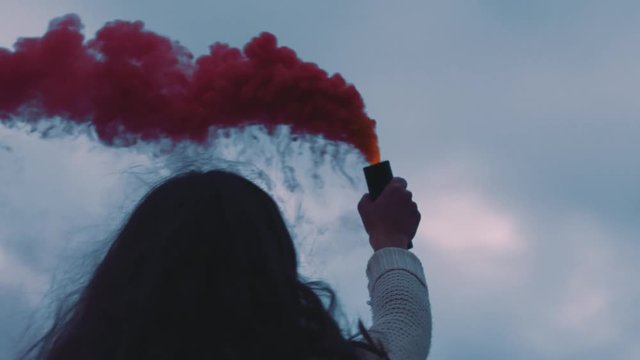 young woman playing with pink smoke grenade dancing on seaside beach enjoying freedom