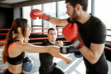 Fototapeta na wymiar Man and woman training to box with personal coach on the boxing ring at the gym