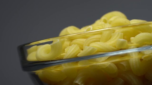 Raw macaroni in rotation. Elbow macaroni. Macaroni rigati close up.  Raw pasta  grey background. Italian cuisine concept.