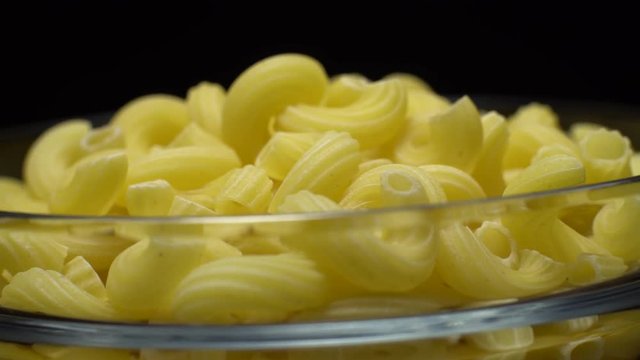 Raw macaroni in rotation. Elbow macaroni. Macaroni rigati close up.  Raw pasta  black background. Italian cuisine concept.