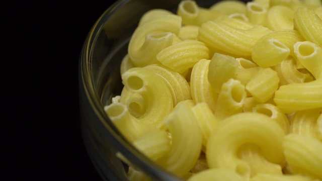Raw macaroni in rotation. Elbow macaroni. Macaroni rigati close up.  Raw pasta  black background. Italian cuisine concept.