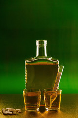 Bottle and glass with whiskey and a thermometer on a green golden background.
