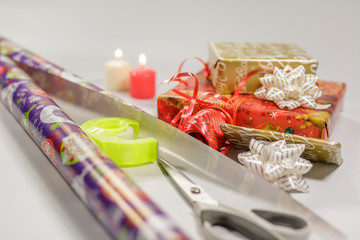Packing Christmas gifts using paper, scissors, tape and ribbons, white background.