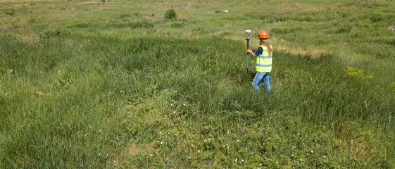 Professional Female Land Surveyor Measures Ground Control Point Using a GPS Rover. Green Field on a...